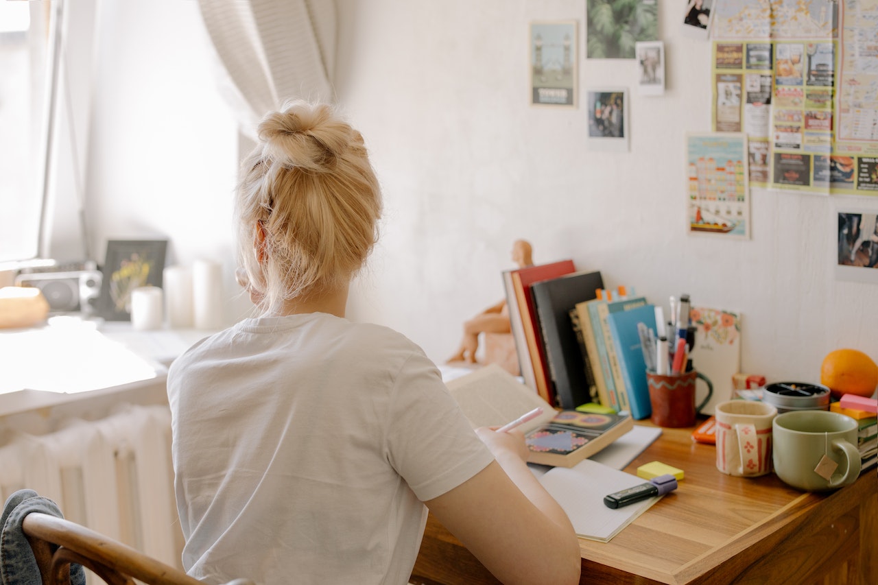 student sitting at desk in dorm looking out of the window and preparing to write in her notebook