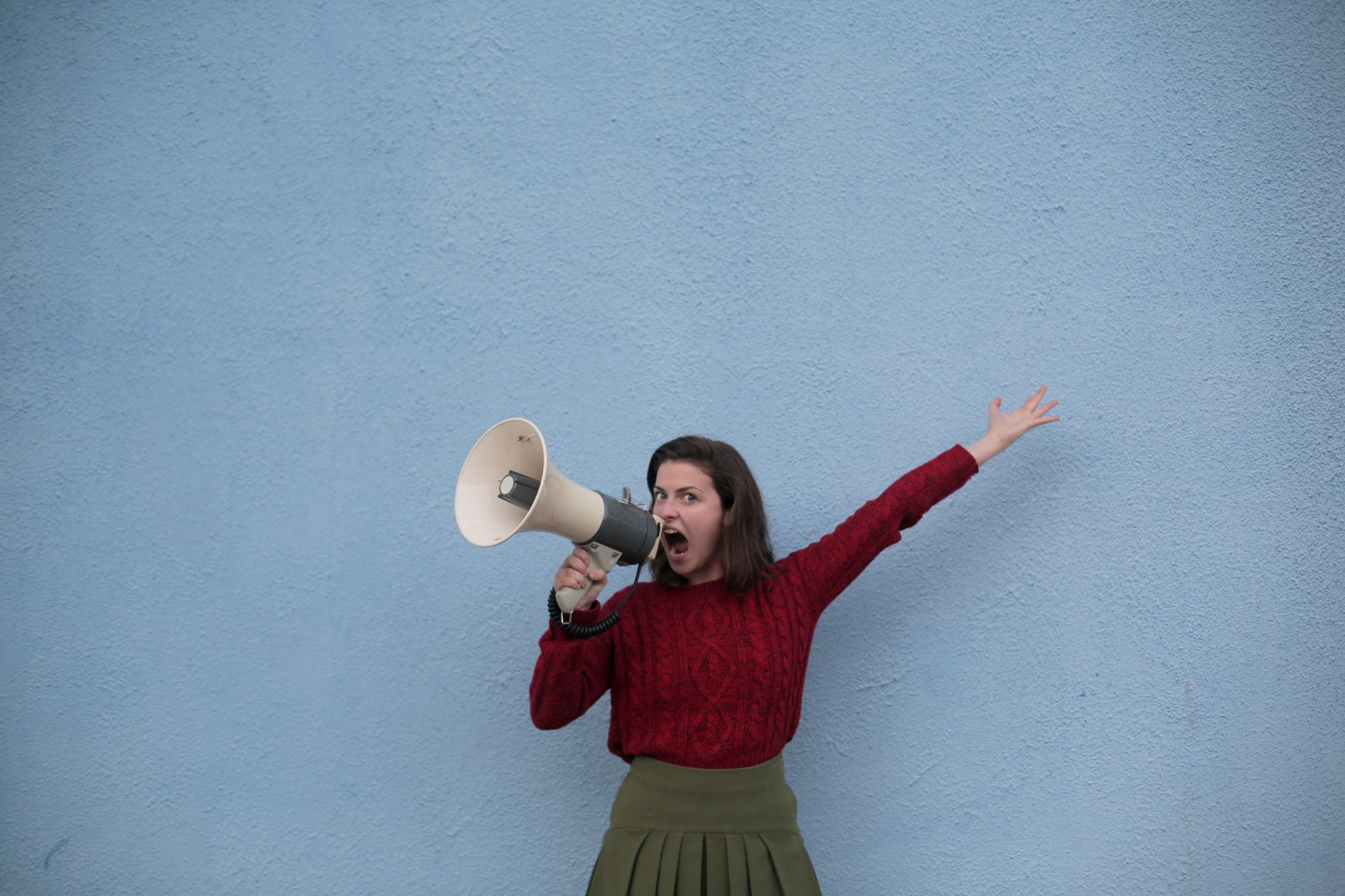 Woman standing in front of a blue wall, shouting into a megaphone