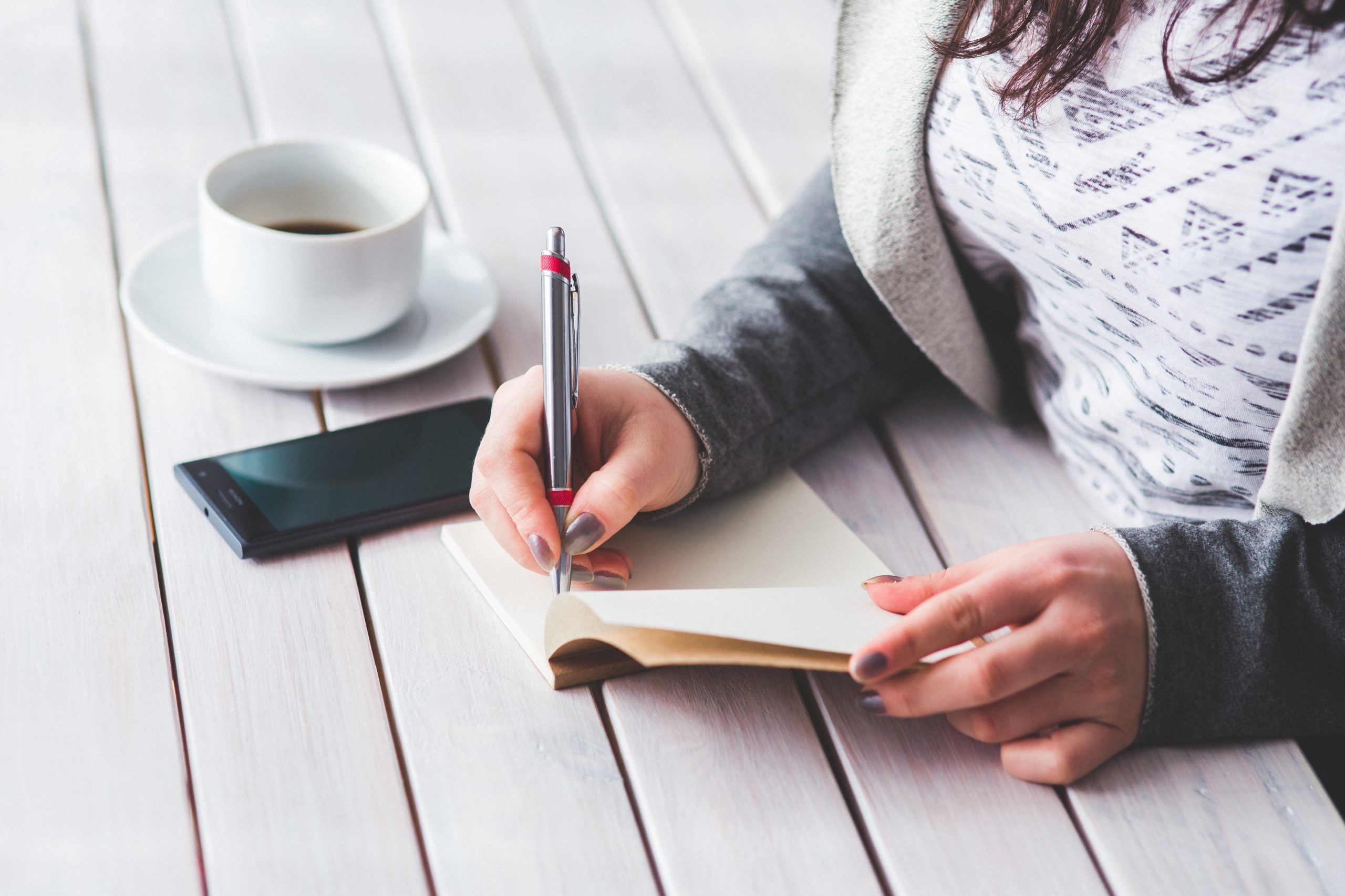 Woman writing in a journal while drinking coffee