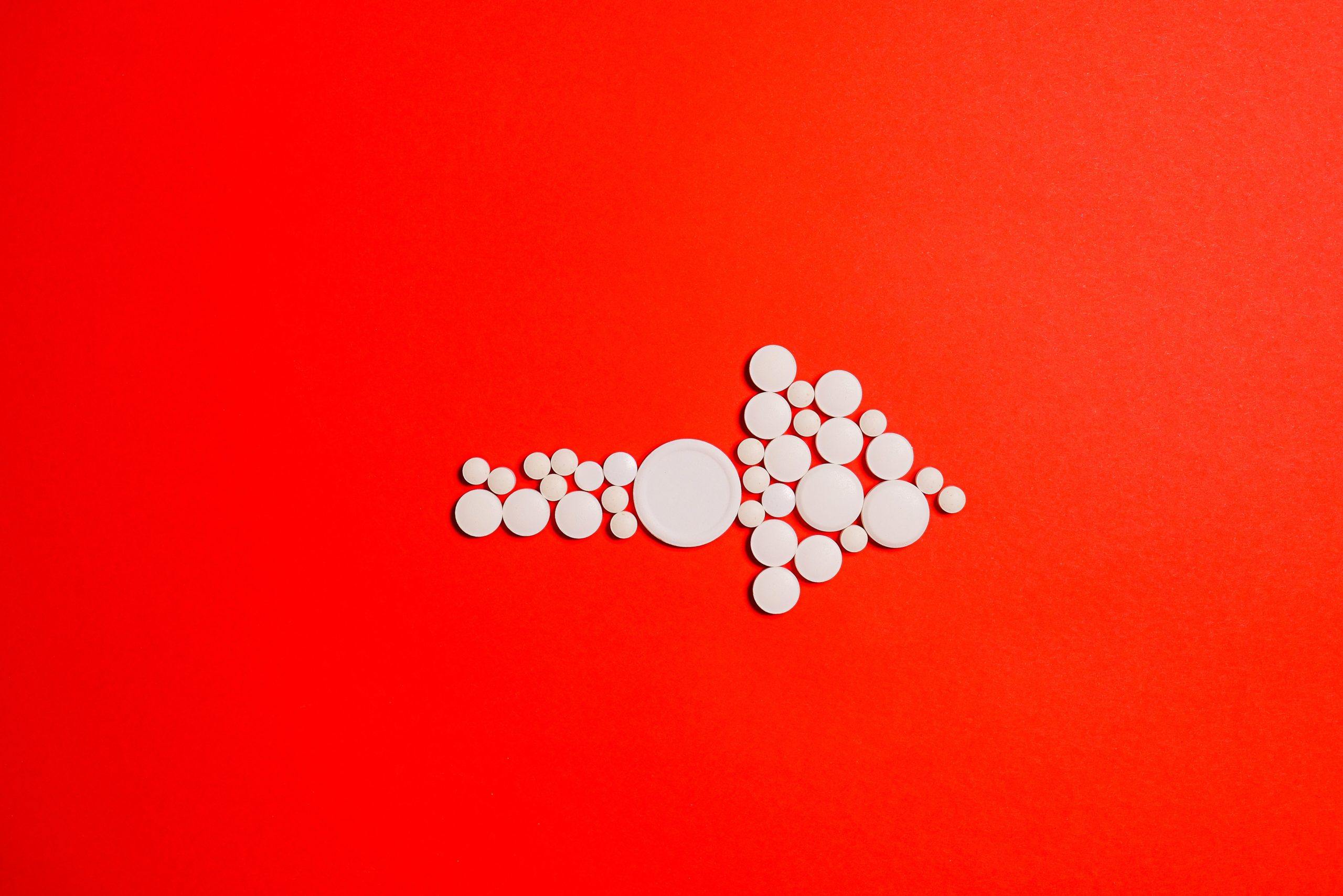 Arrow pointing right made out of pills on a red background