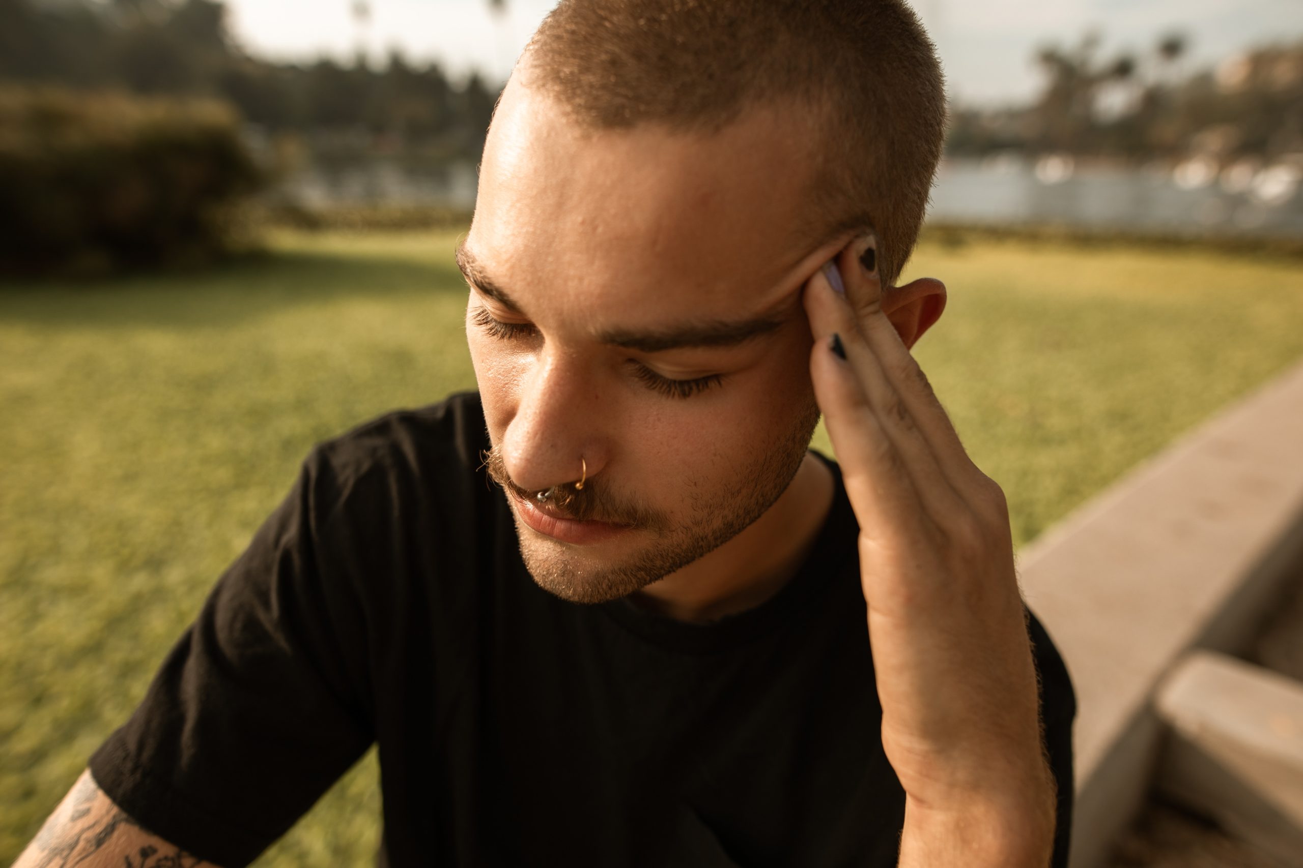Man with his hand massaging his temple, sitting outside with his eyes closed