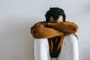 Man sitting against a white wall with his head in his hands