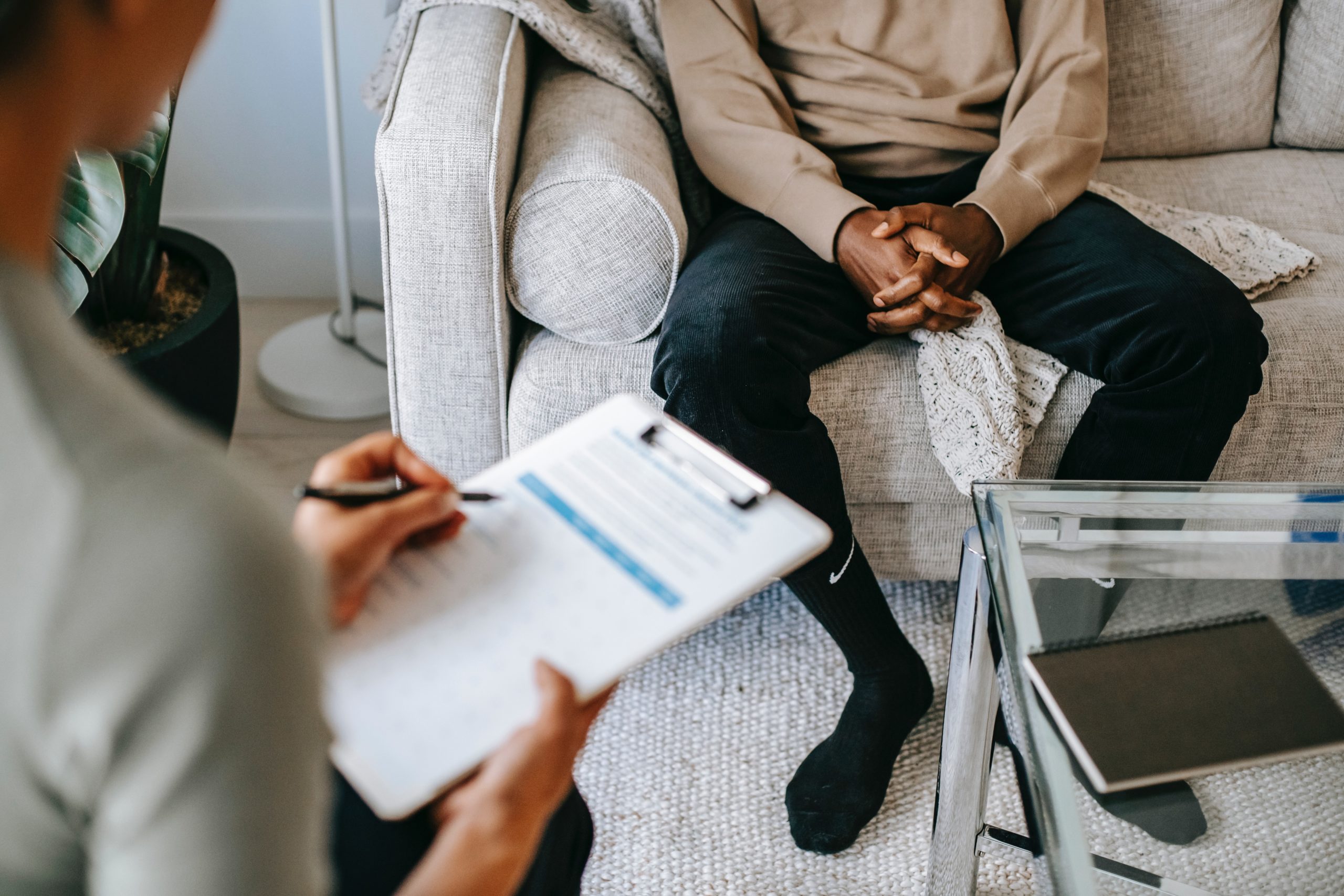 body of person sitting with hands clasped between his legs while sitting on a couch talking to therapist