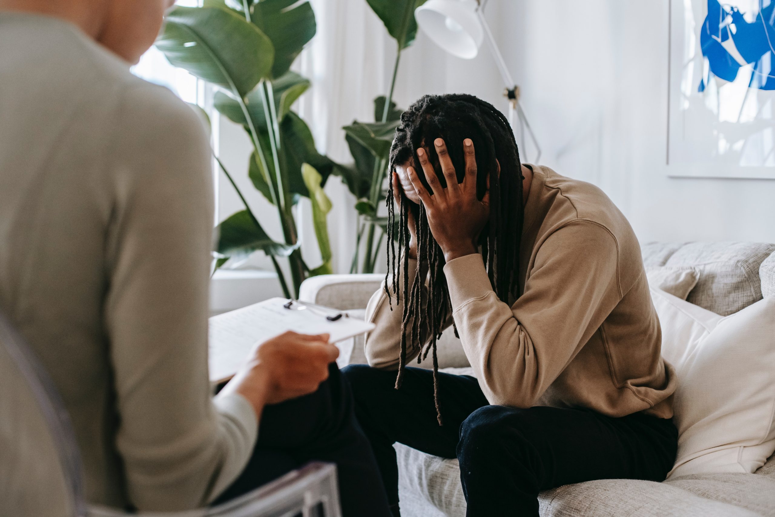 Man sitting on couch talking with therapist looking very upset and hands covering his face