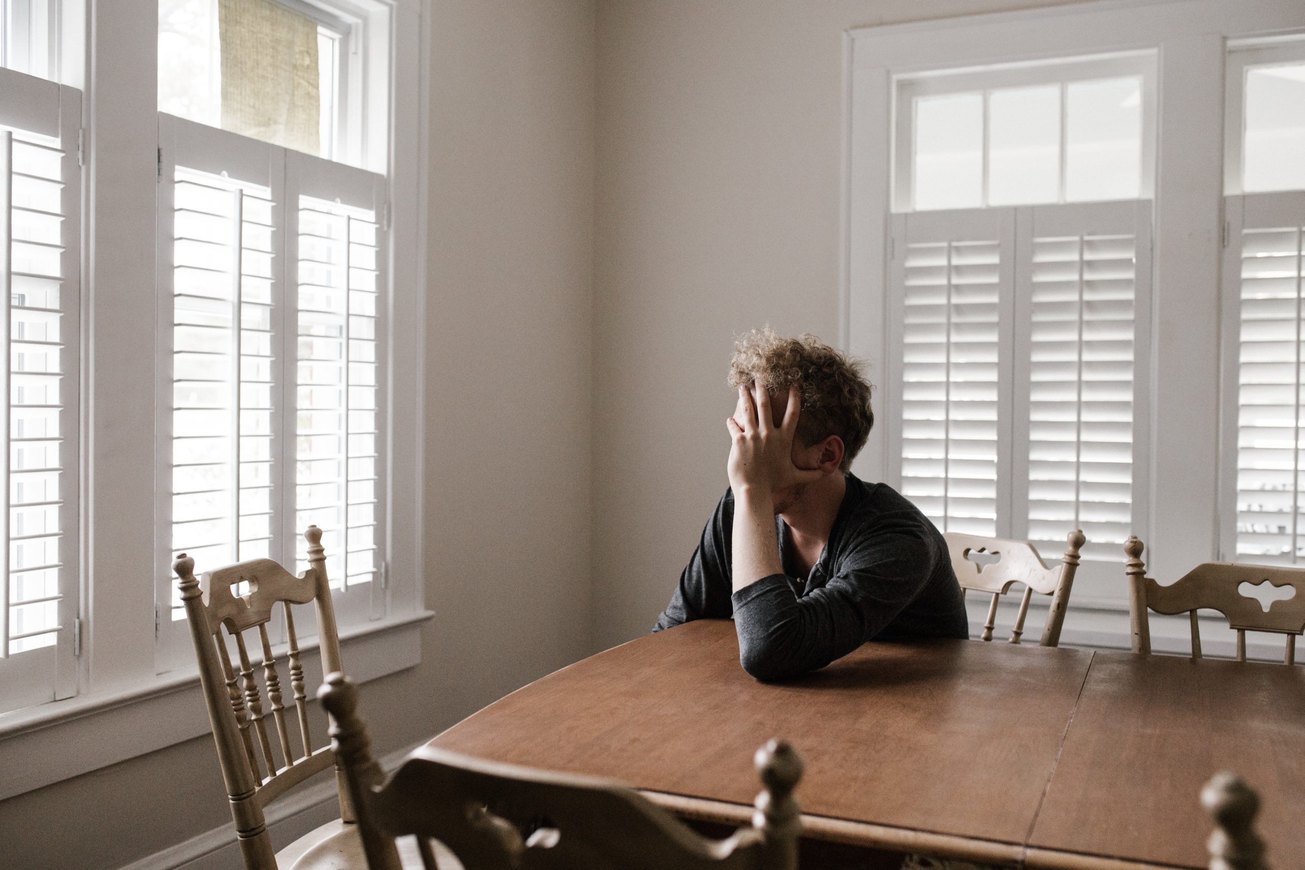 guy sitting at the table, facing a window, with his hand on his head