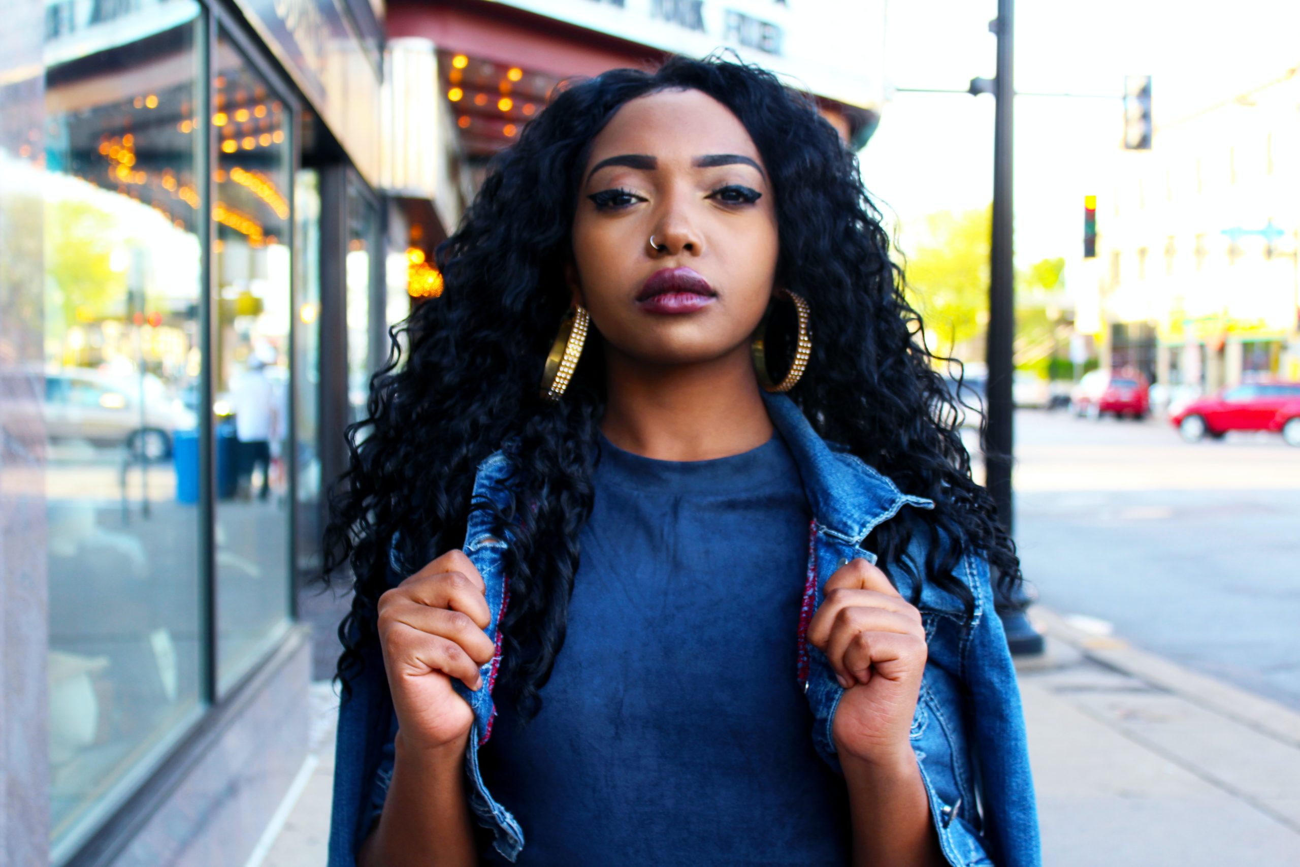 Woman With Curly Hair Wearing Large Hoop Earrings and Denim Jacket on City Street.