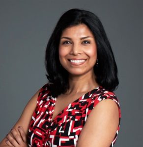 brown complexion woman with shoulder length black hair smiling, arms crossed, wearing red, black and white checkered blouse