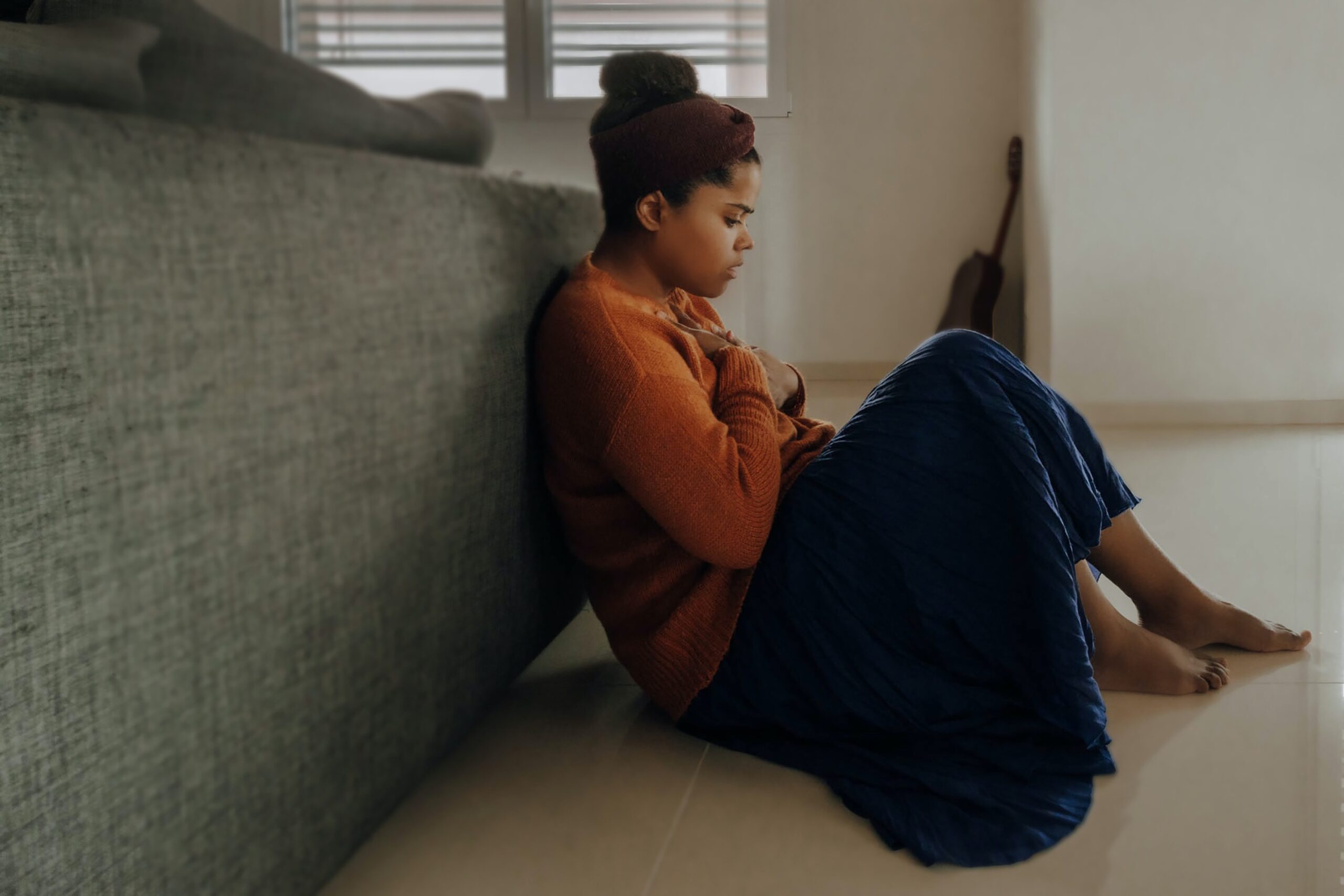 young woman sitting on the floor of her bedroom looking worried
