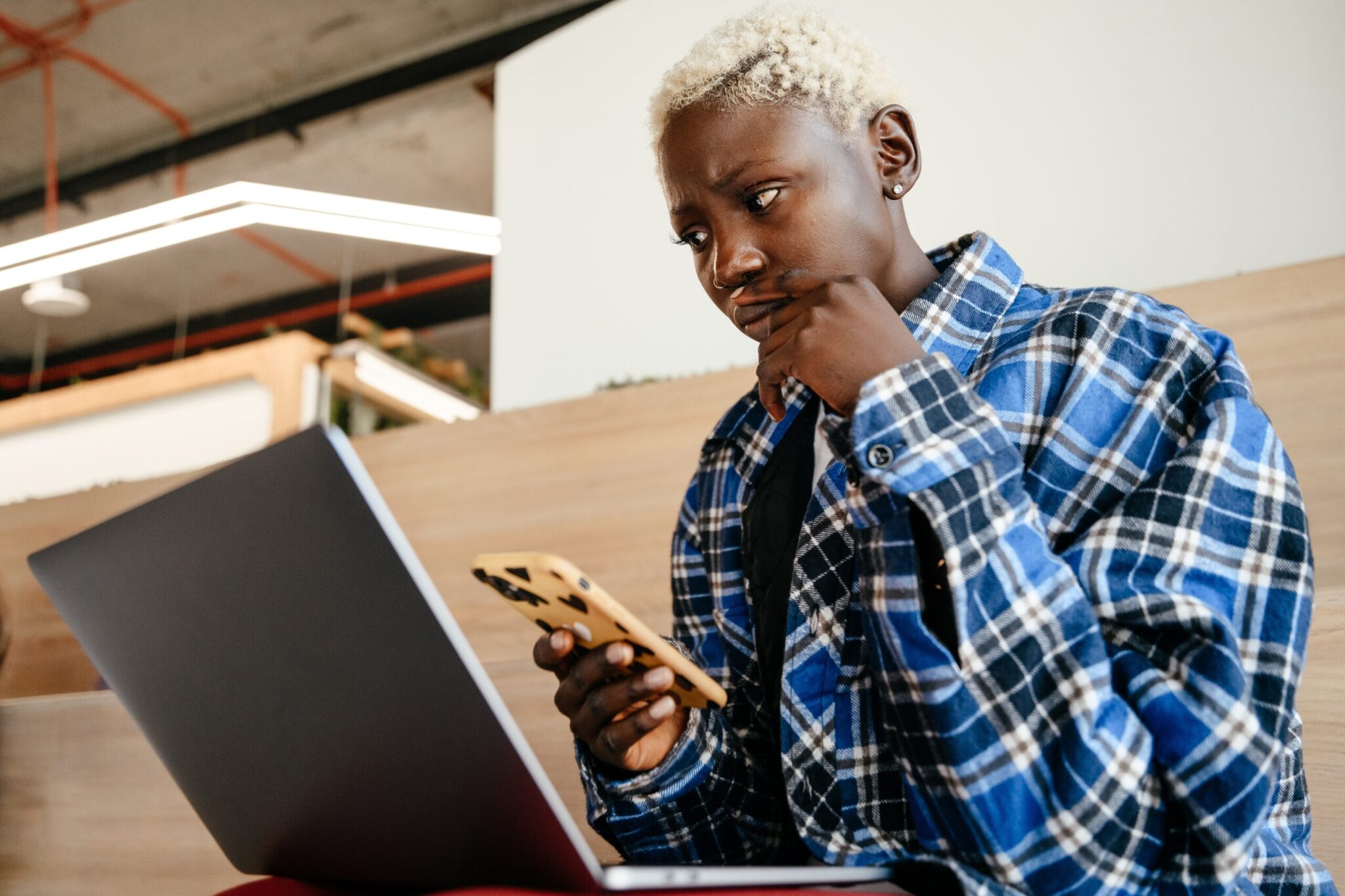 young person staring at a computer screen with a concerned look while holding a cellphone