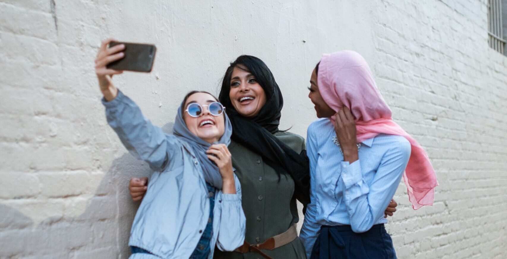 three young women taking a selfie outside with a brick wall behind them