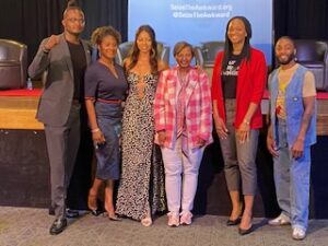 Black students and panelists from standing in college auditorium smiling with stage behind them