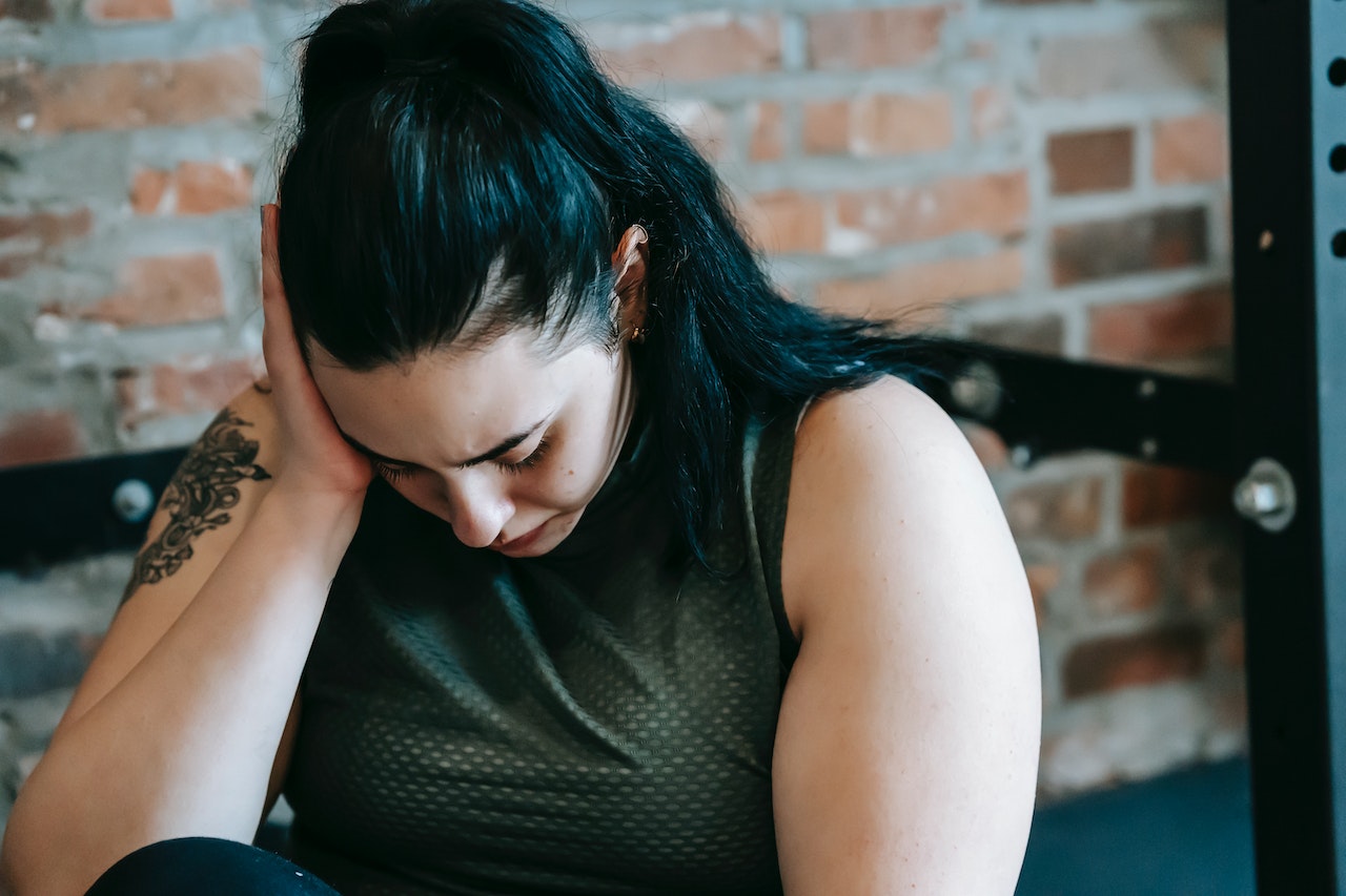 young woman sitting on a bench with her head down, one arm on her face, looking upset over her past trauma