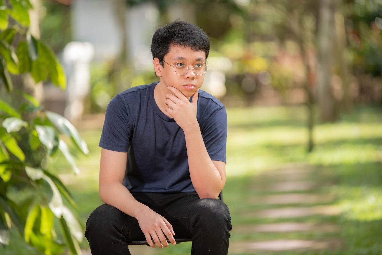 young asian man sitting outside thinking