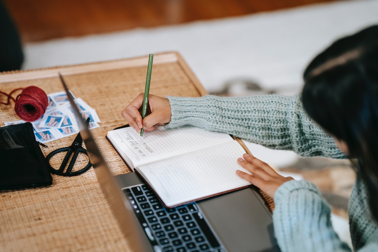 student sitting at a desk writing in a notebook, with laptop open; planning on how to address mental health challenges on campus