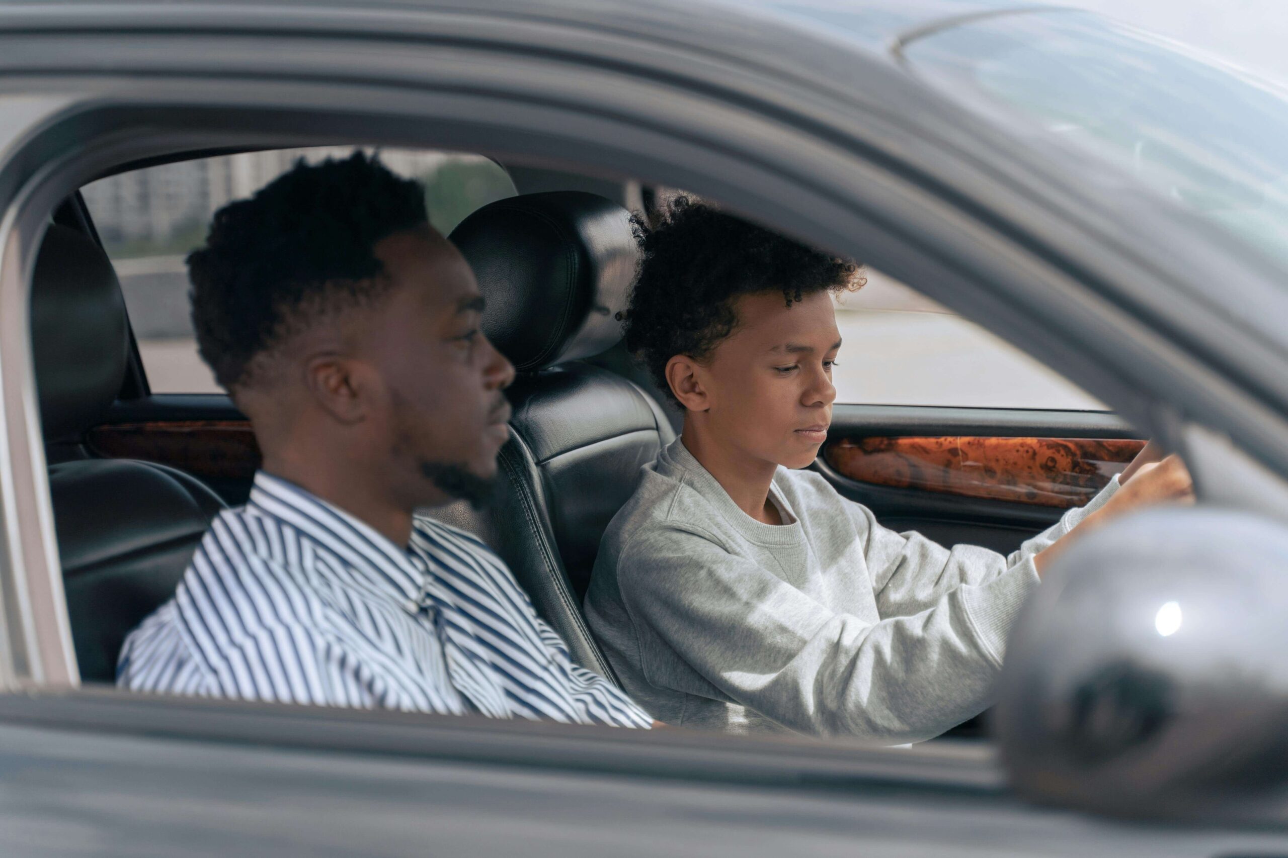 A Black father and his son sit in a car together.