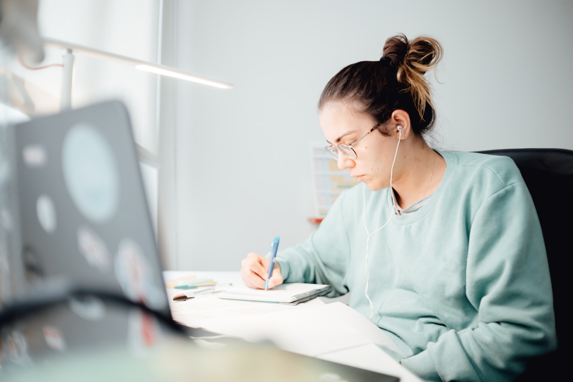 college student sitting at desk, facing computer screen while focused on writing in notebook