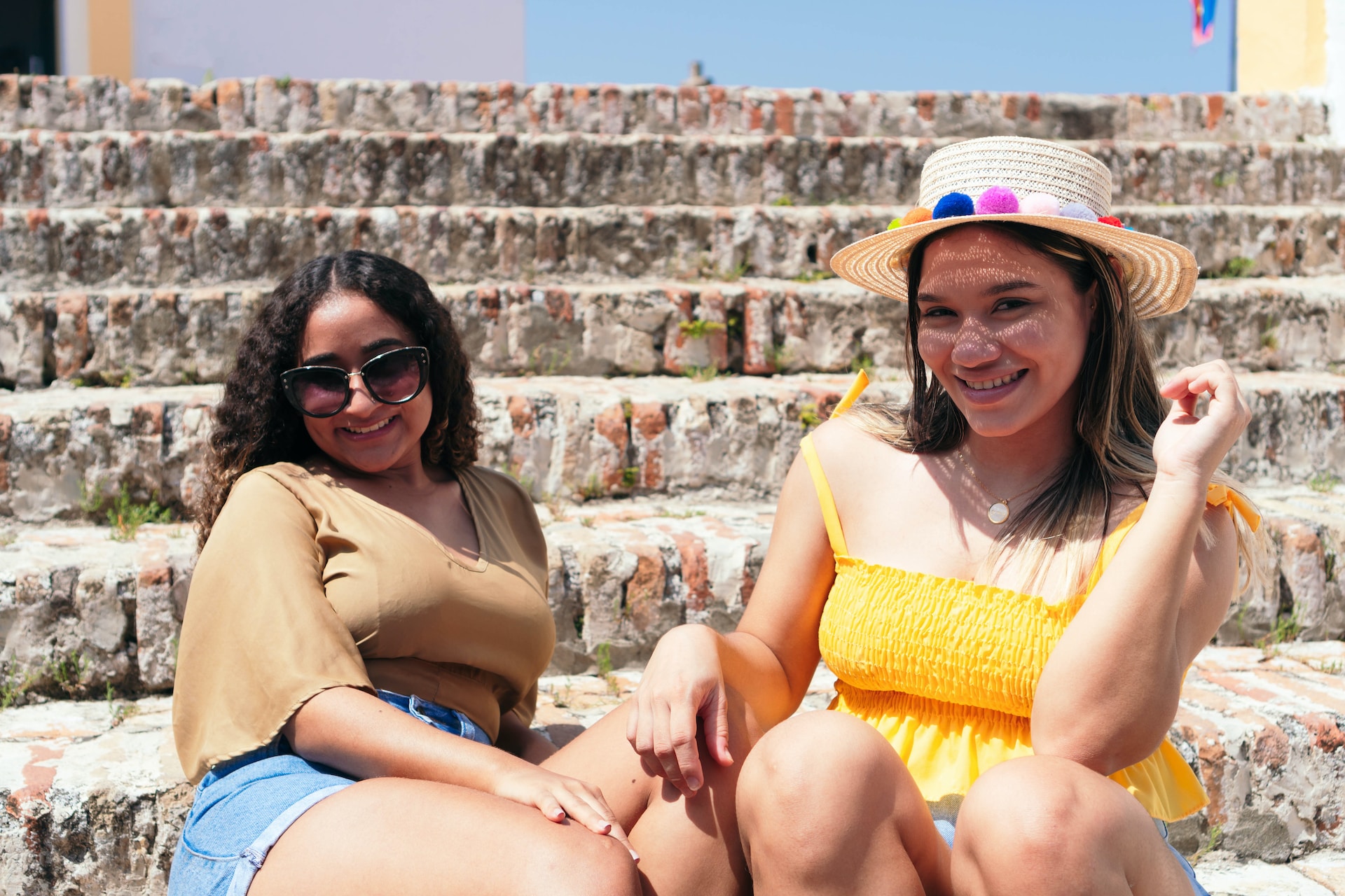latine college friends smiling while sitting outside in the sun on steps together