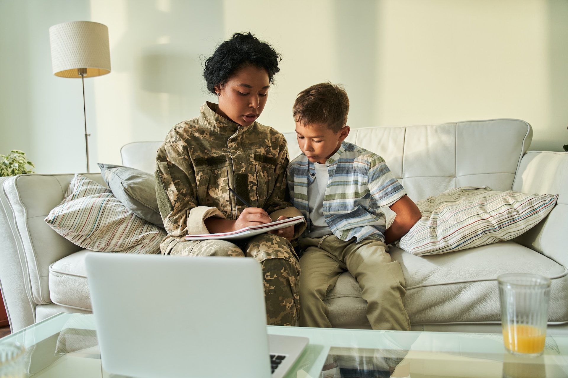 Veteran college student and parent sitting on couch with toddler and writing in notebook