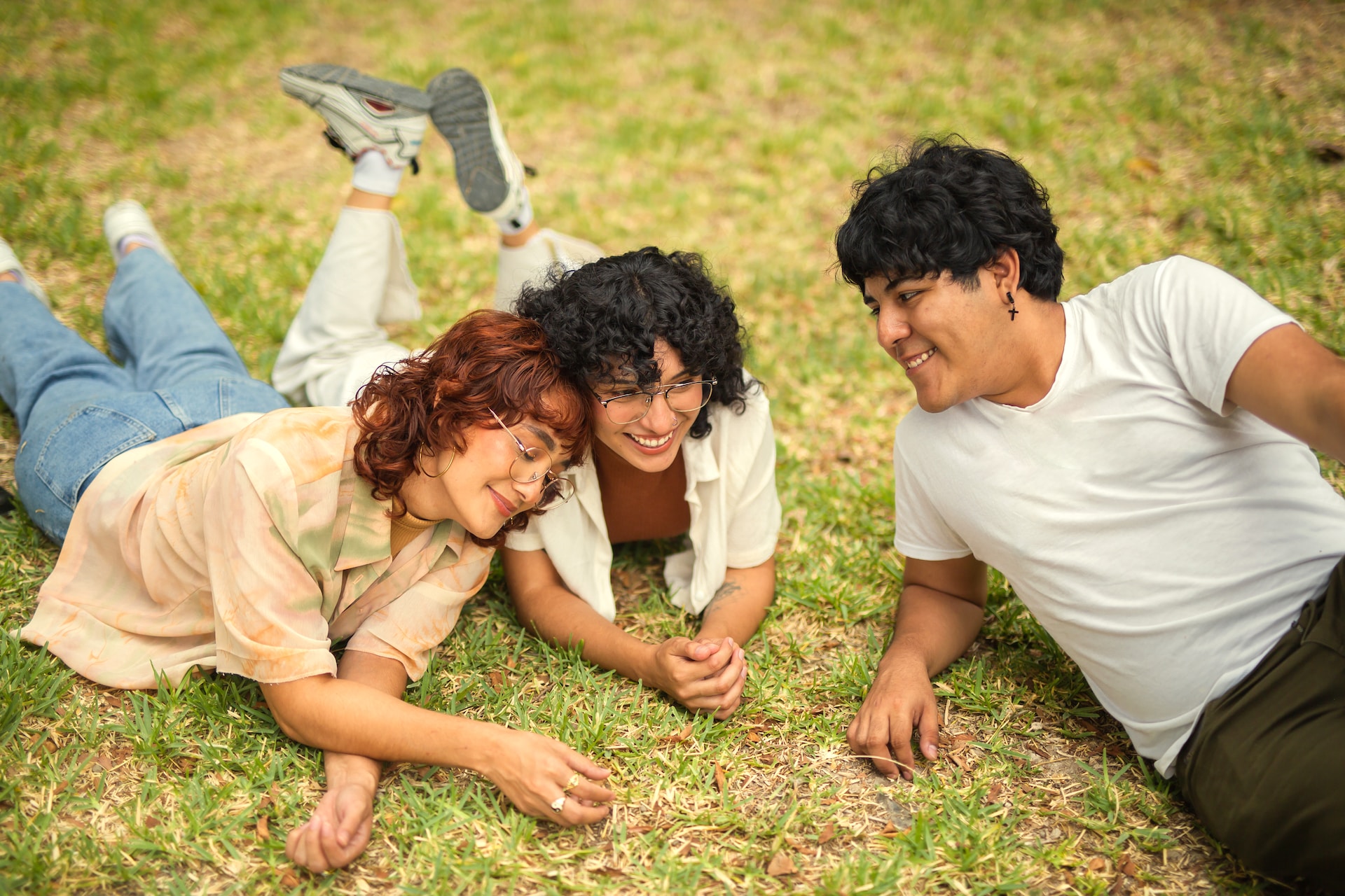 college friends laying out on the park grass smiling and talking
