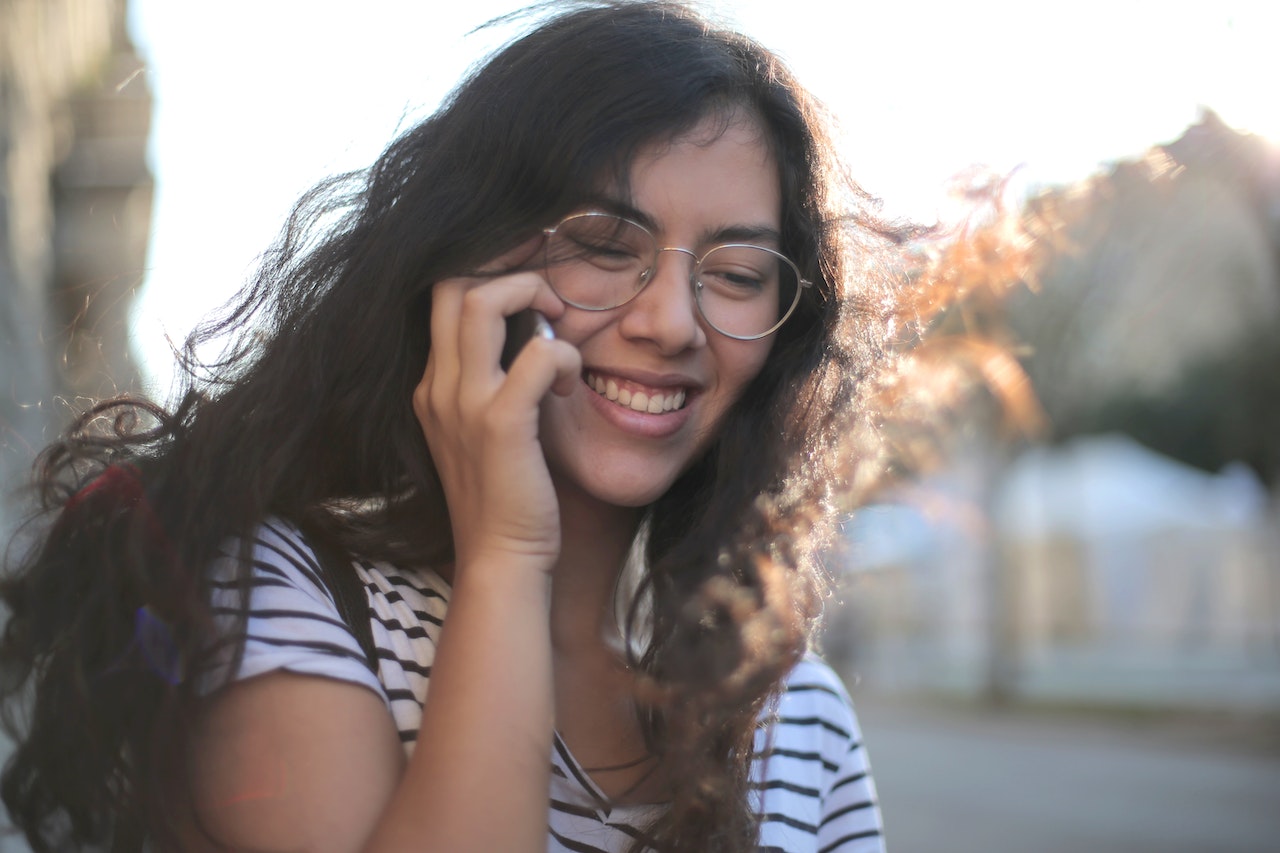 homesick college student smiling while talking on the her mobile phone