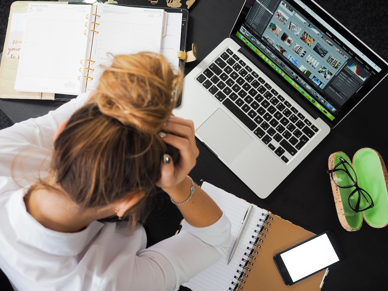 student sitting at table with hands covering face, laptop open, notebook, phone and glasses on table, dealing with failure