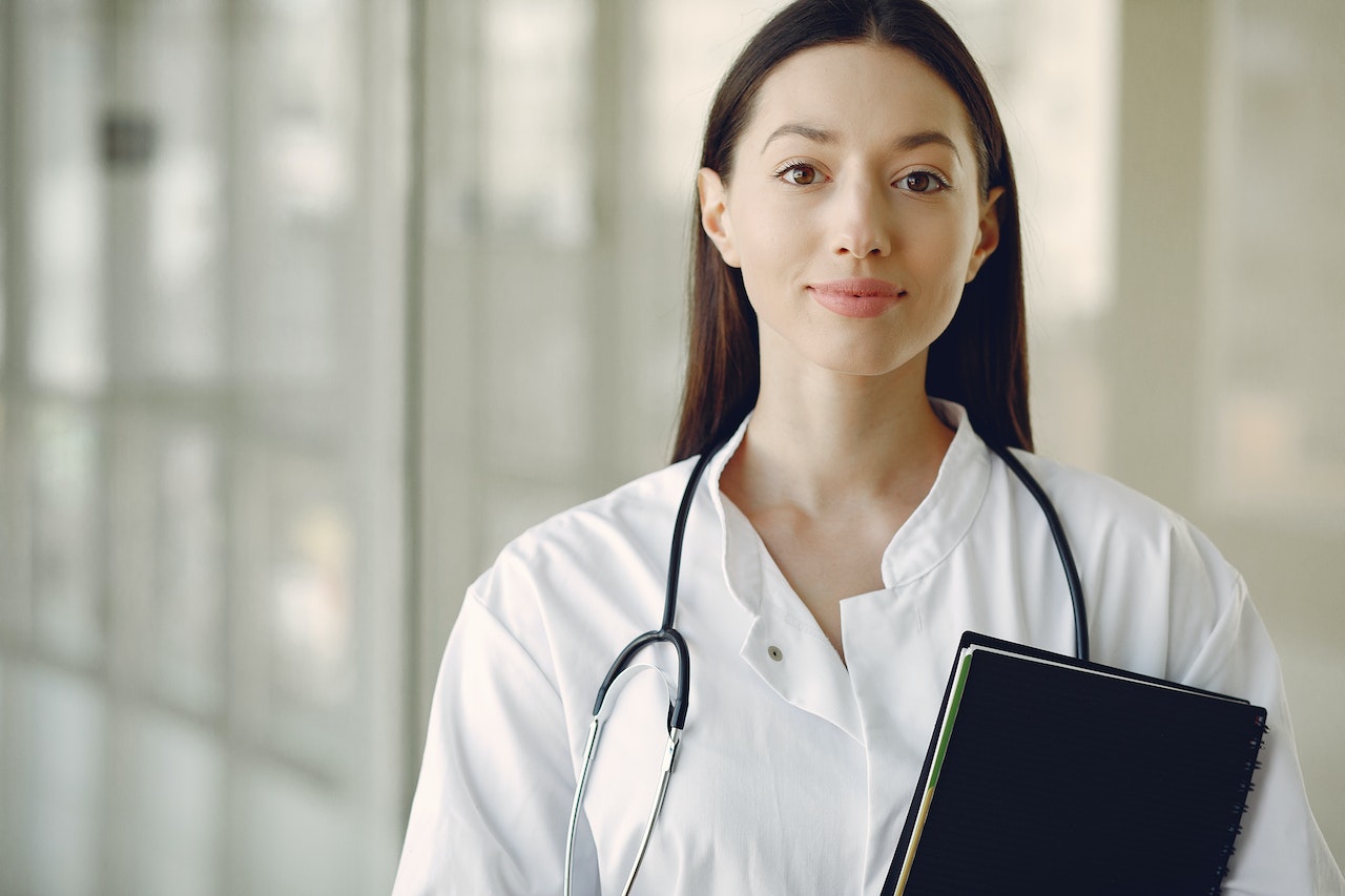 young doctor standing with stethoscope around her neck and notebook in hand