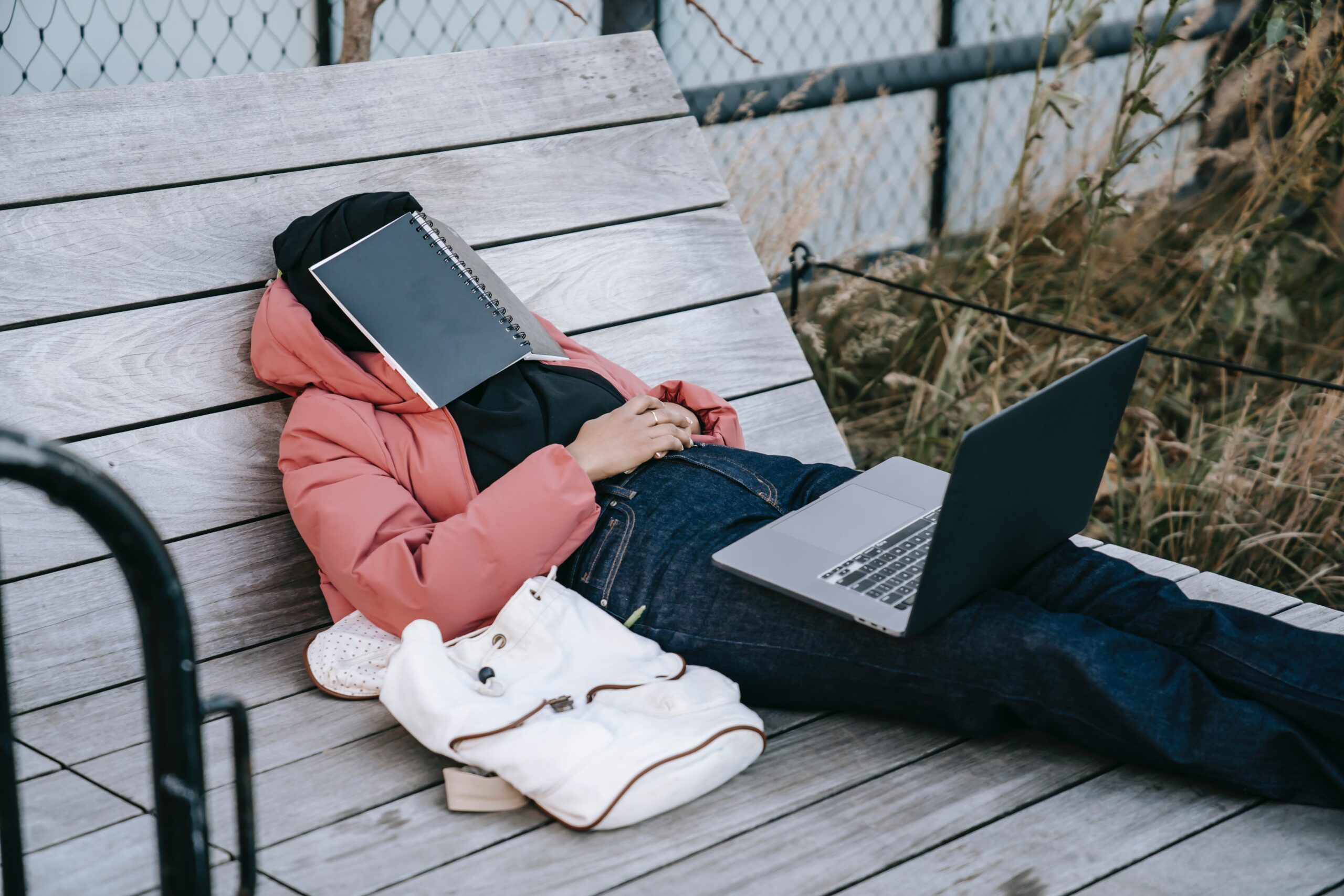 A stressed student with a book over her face and a laptop sitting on her legs