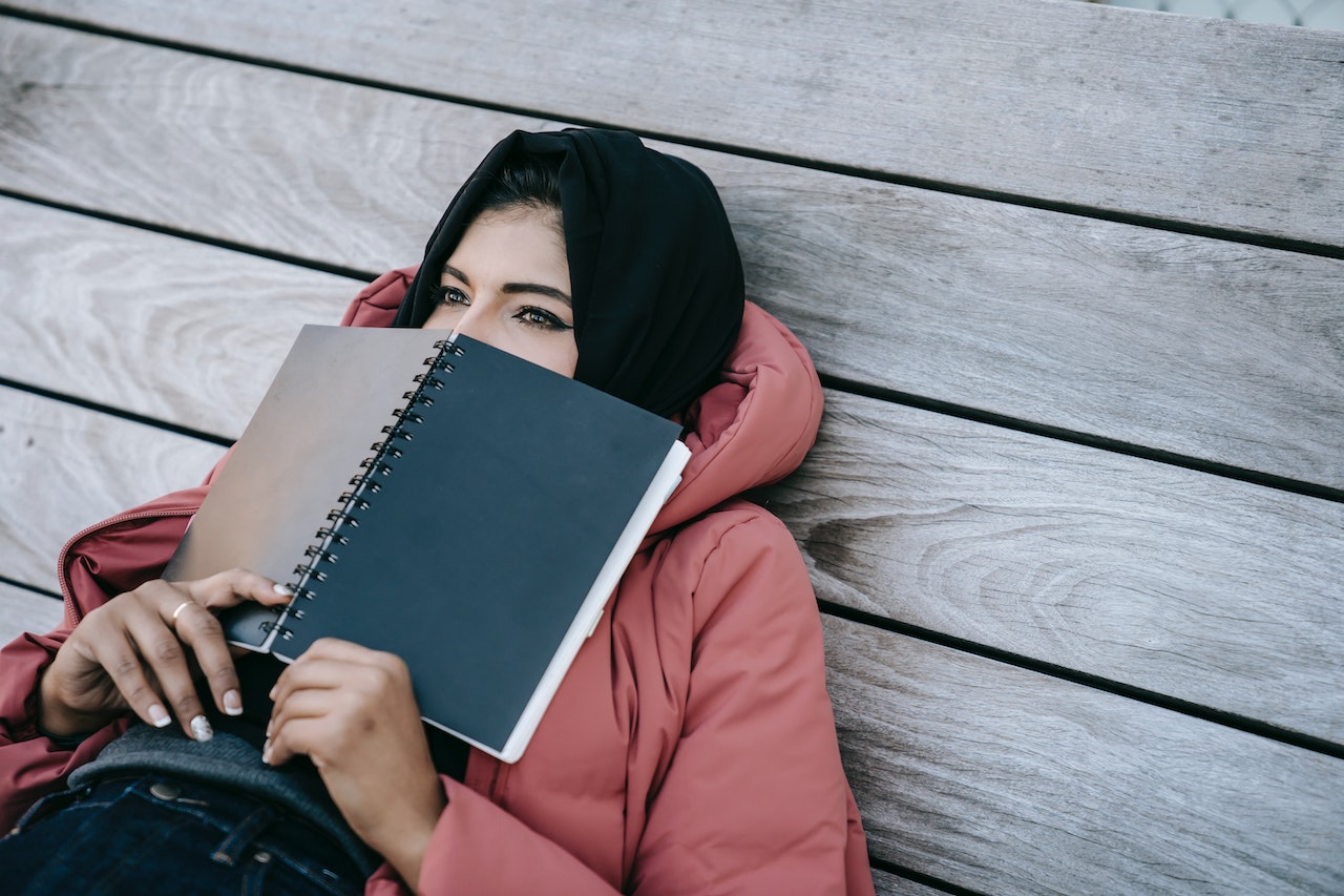 young woman laying down on deck deep in thought holding an open book over her nose,