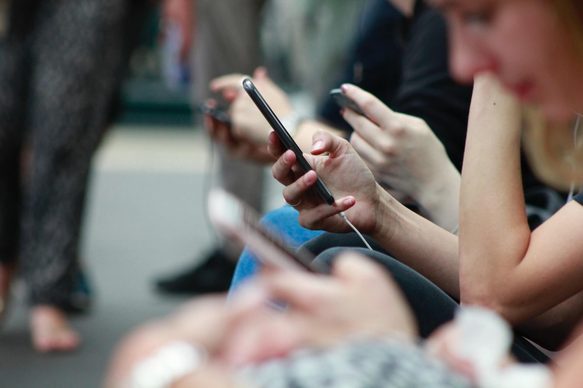 Several people holding and looking at their phones in a busy public setting