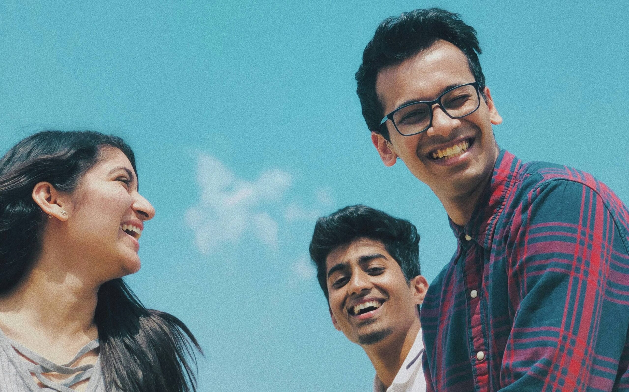 A group of friends laughing and smiling while standing outside on a blue-skied day.
