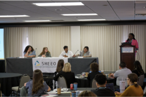 Moderator standing with panel of students