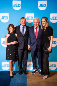 two couples standing side by side in front a blue backdrop with jed logo on them