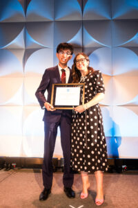 young man and woman standing together on stage holding a rectangular shaped award