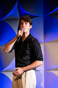 man wearing black button up shirt and khaki pants with microphone to his mouth while singing on stage