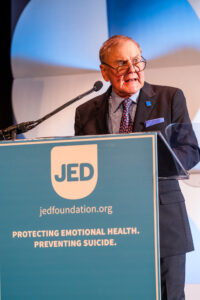 man wearing glasses standing at podium with microphone in front of him