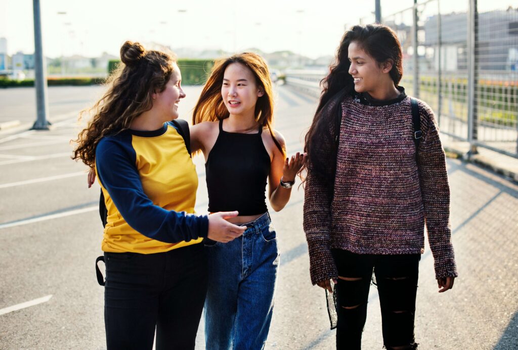 Three young people walk through a parking lot while engaging in a lively conversation.