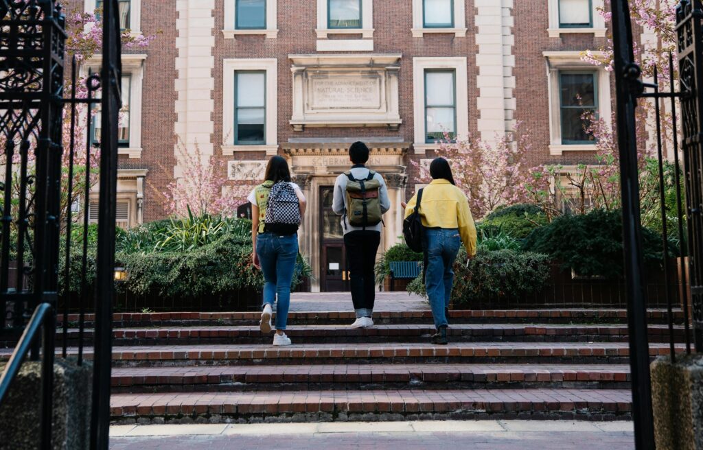 Three students walk up the steps to a building on their college campus.