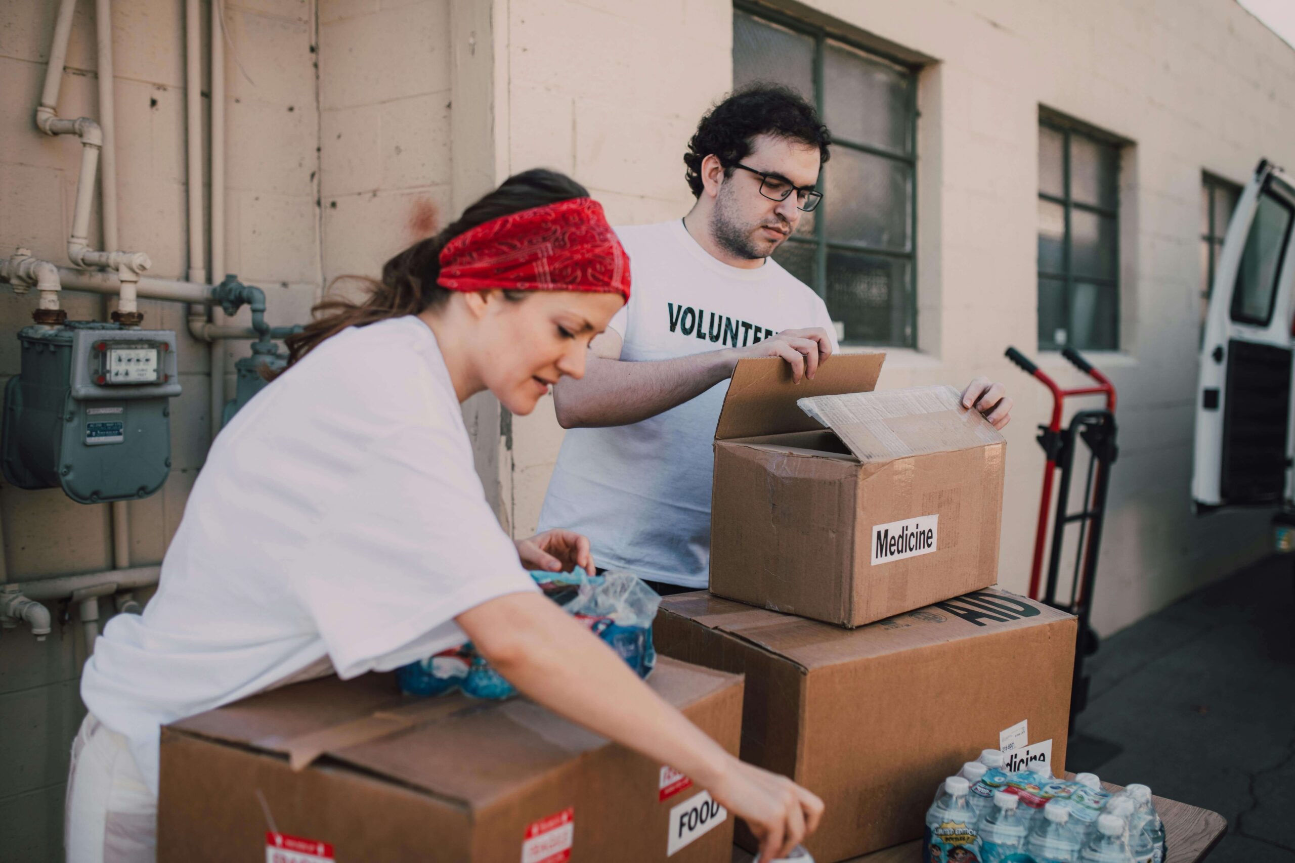 Two young people unpack water bottles and a box of medicine at a volunteer event.