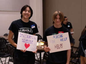 Two students at Chandler Unified School District's Student Health Summit holding signs that read "It's okay to be yourself" and "Asking for help helps."