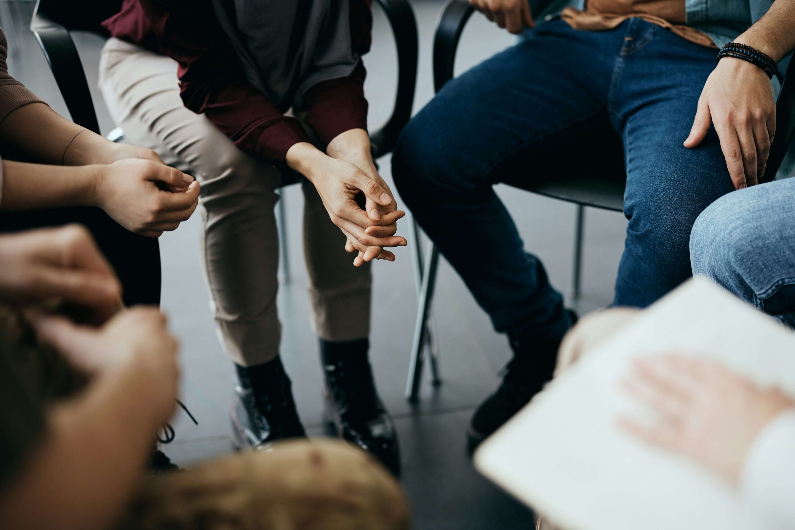 A group sitting together in a circle, leaning on their knees with their hands clasped.