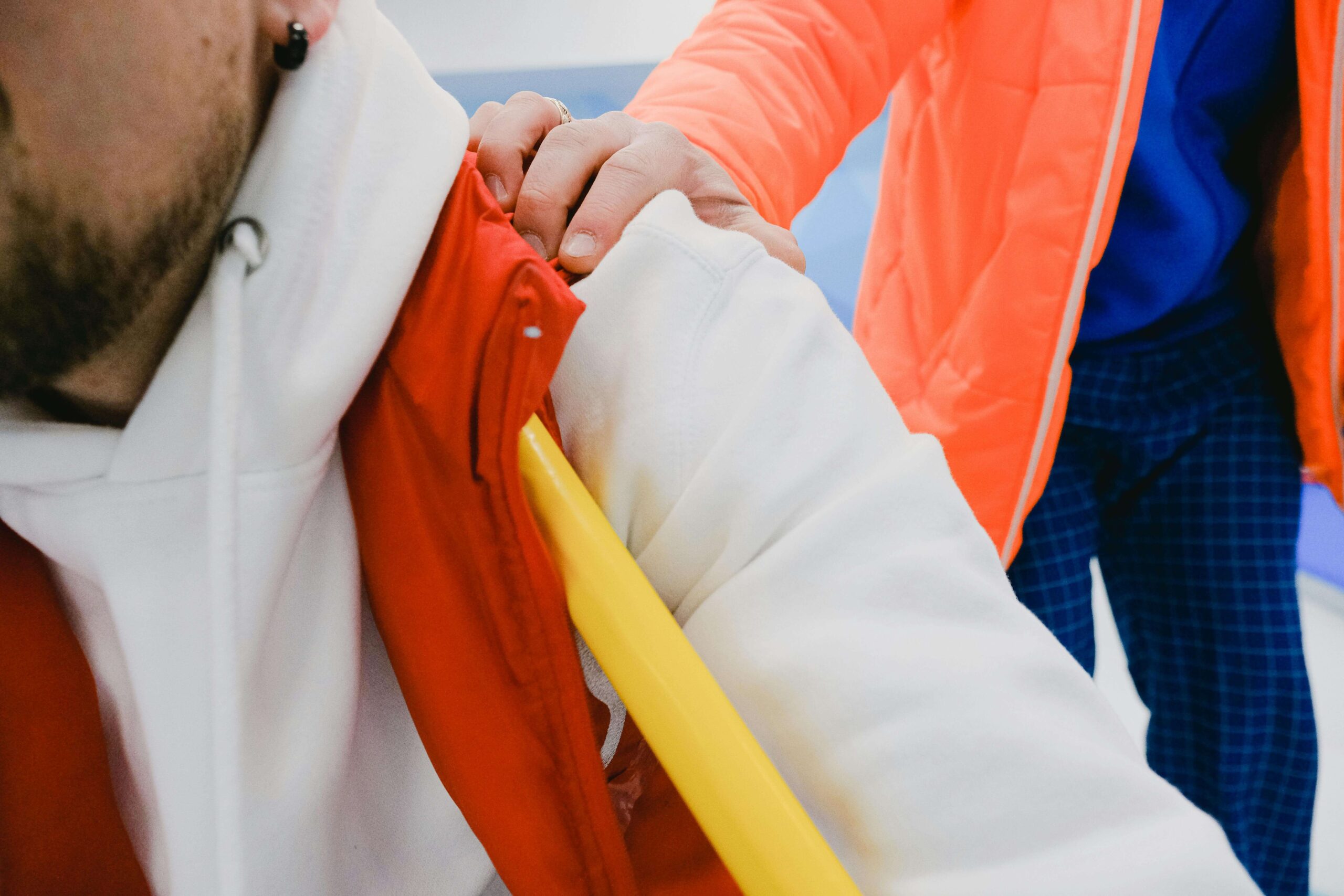 A person wearing a bright orange jacket puts their hand on someone sitting down wearing a red vest.