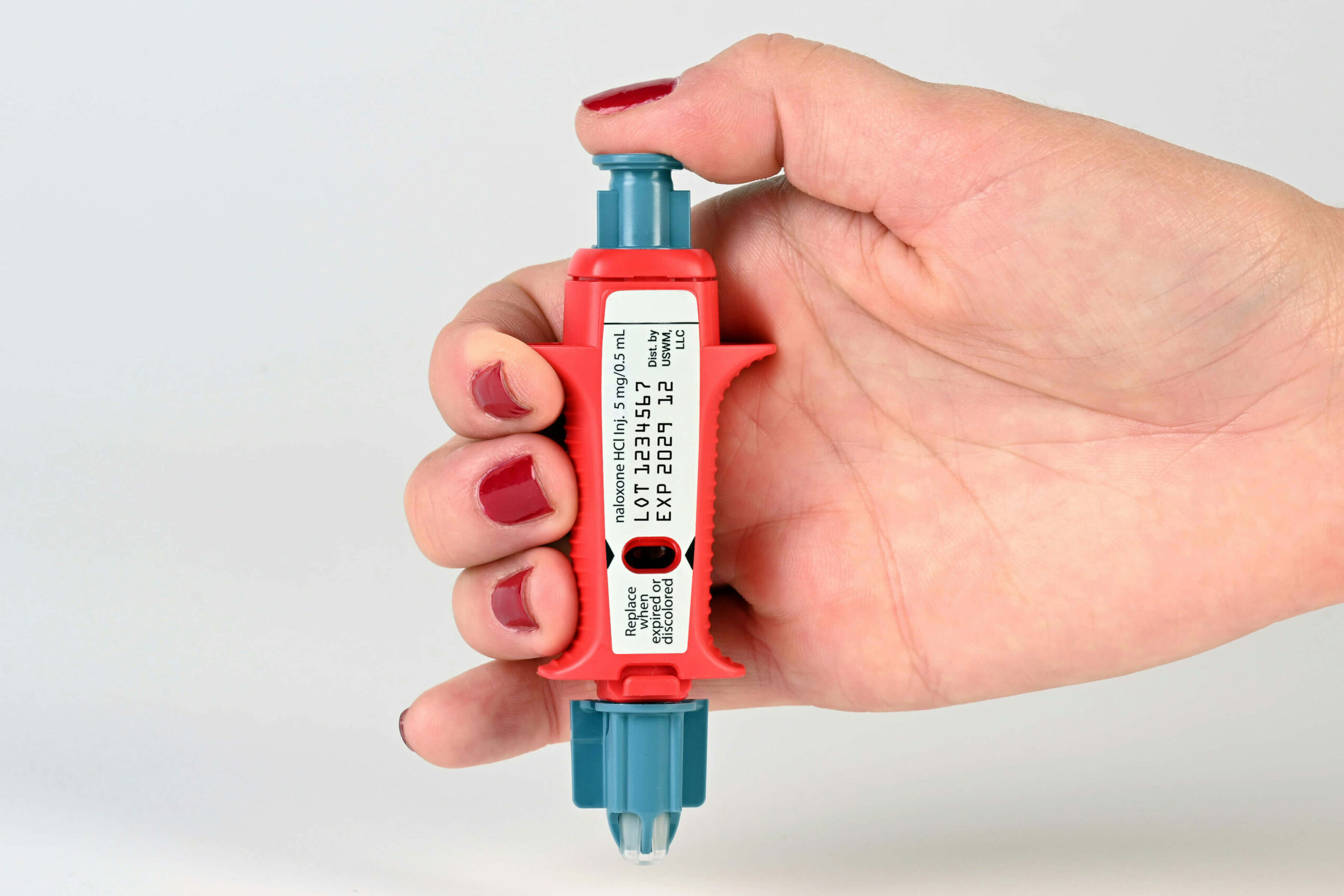 A hand holding naloxone nasal spray contained in blue and red packaging with a white label.