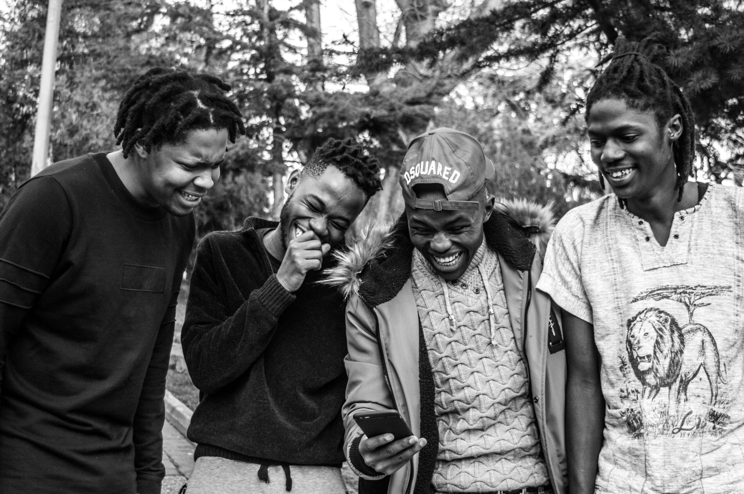 A group of young Black men gathered outside around a phone and laughing.